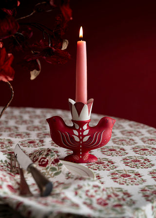 Red candle holder with a pink candle on a patterned tablecloth