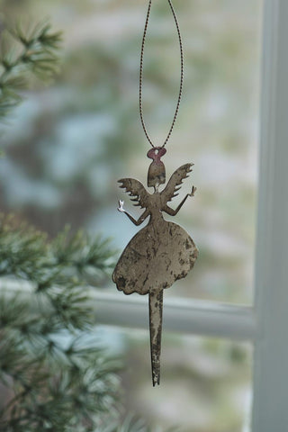 Gold angel ornament holding hearts hanging on a twisted cord against a blurred window and pine branch background