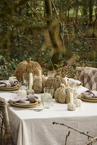 Woven seagrass and rattan pumpkins arranged on an outdoor table set with linen napkins, candles, and small ceramic pumpkins