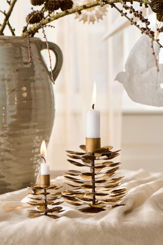 Two lit candles in brass pinecone candle holders beside a ceramic pitcher with a decorated branch arrangement