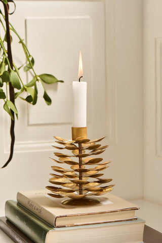 Lit white candle in a gold brass pinecone candle holder standing on a stack of books beside a hanging sprig of mistletoe