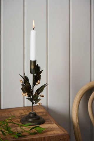 Close-up of the metal leaf and wooden bead candle holder with a lit white candle on a wooden table corner, with a mistletoe sprig in the foreground