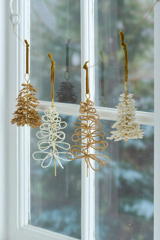 White and gold beaded Christmas tree ornaments hanging from mustard velvet ribbons in a window, alongside looped wire tree ornaments