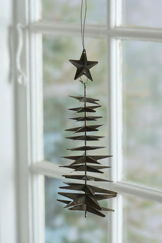 Weathered silver metal star Christmas tree ornament hanging in front of a white-framed window