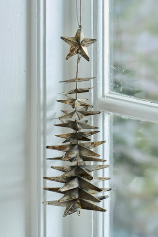 Close-up of a weathered silver metal star Christmas tree ornament with a star topper hanging beside a window frame