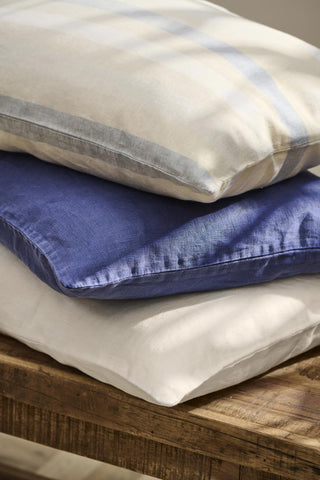 Stack of striped and plain cotton cushions in cream, indigo, and blue on a rustic wooden bench