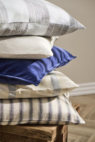 Stack of striped cotton cushions in cream, grey, and charcoal on a rustic wooden crate
