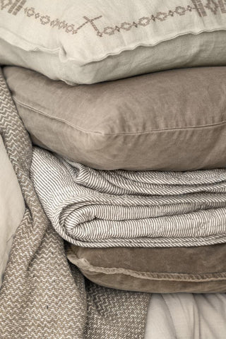 Close-up of a striped quilted throw folded over layered grey, taupe and cream cushions on a wicker chair