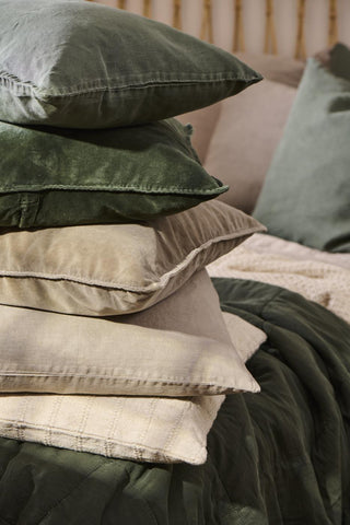 Stack of layered cushions in green, taupe and cream tones with a striped quilted throw and other textiles