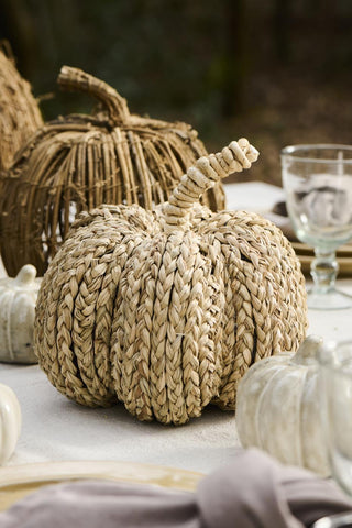 Braided seagrass pumpkin on an outdoor autumn table setting with candles, glassware, and a woven rattan pumpkin in the background