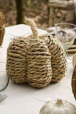 Woven seagrass deco pumpkin with twisted stem set on a table beside glassware, cutlery, and a small white ceramic pumpkin