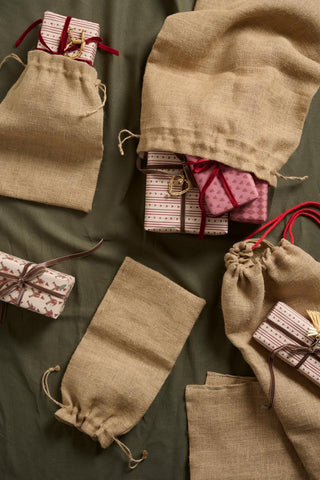 Jute drawstring gift sacks and wrapped presents with ribbons and gift tags arranged on an olive green tablecloth