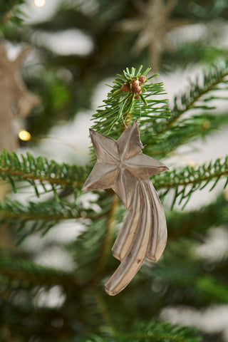 Silver metal shooting star ornament hanging from a Christmas tree branch with pine needles and soft twinkling lights