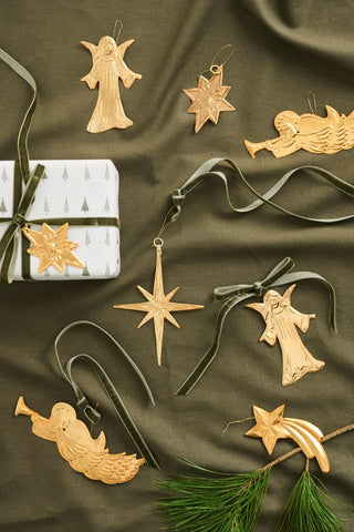Gold angel, star, and shooting star ornaments displayed on an olive green fabric with a wrapped gift, ribbon, and pine branch