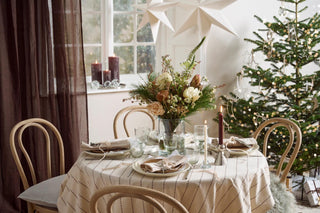 Christmas dining table with large paper stars hanging overhead, a floral centerpiece, burgundy candles, and a decorated tree in the background