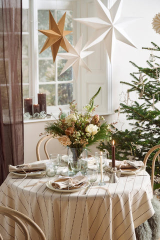 Christmas room with large gold and white paper stars suspended above a set dining table and a decorated tree