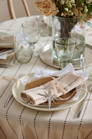 Close-up of a place setting with a silver oblong star ornament tied with ribbon on a folded linen napkin