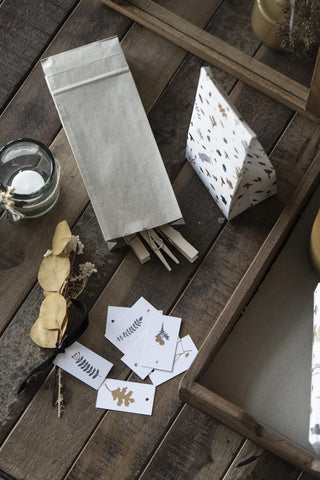 Kraft paper gift bag and patterned gift bag with dried flowers, gift tags, and clothespins on a rustic wooden tray