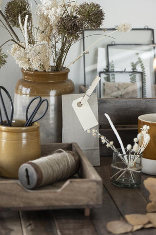 Kraft paper gift bag on a rustic table beside a stoneware vase of dried flowers and a blank gift tag