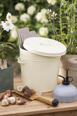 Kraft paper bags holding flower bulbs beside a cream metal storage bucket and garden tools