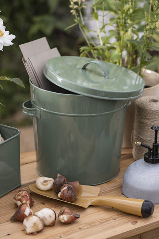 Kraft paper bags holding flower bulbs beside a sage green metal storage bucket and garden tools