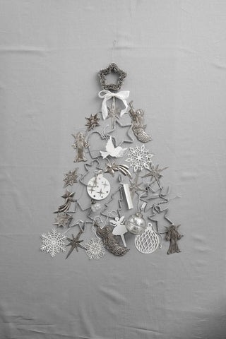 Silver beaded star ornament topping a Christmas tree shape made entirely of assorted silver and white paper and metal ornaments laid flat on a grey cloth
