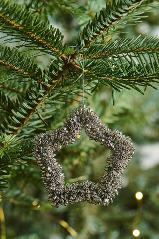 Silver beaded star ornament hanging from a wire loop on a Christmas tree branch with string lights