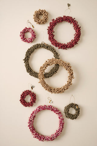 Collection of wooden bead wreaths in natural, olive green, burgundy, and pink tones in varying sizes hanging on a wall