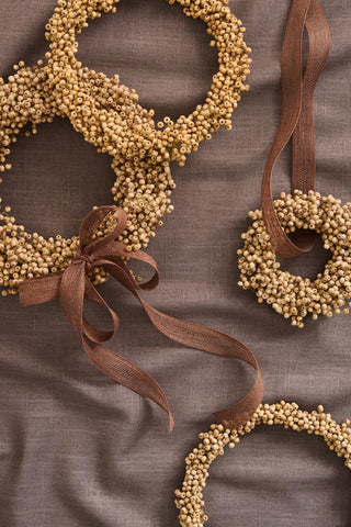 Natural wooden bead wreaths tied with a brown ribbon bow, laid flat on brown linen fabric